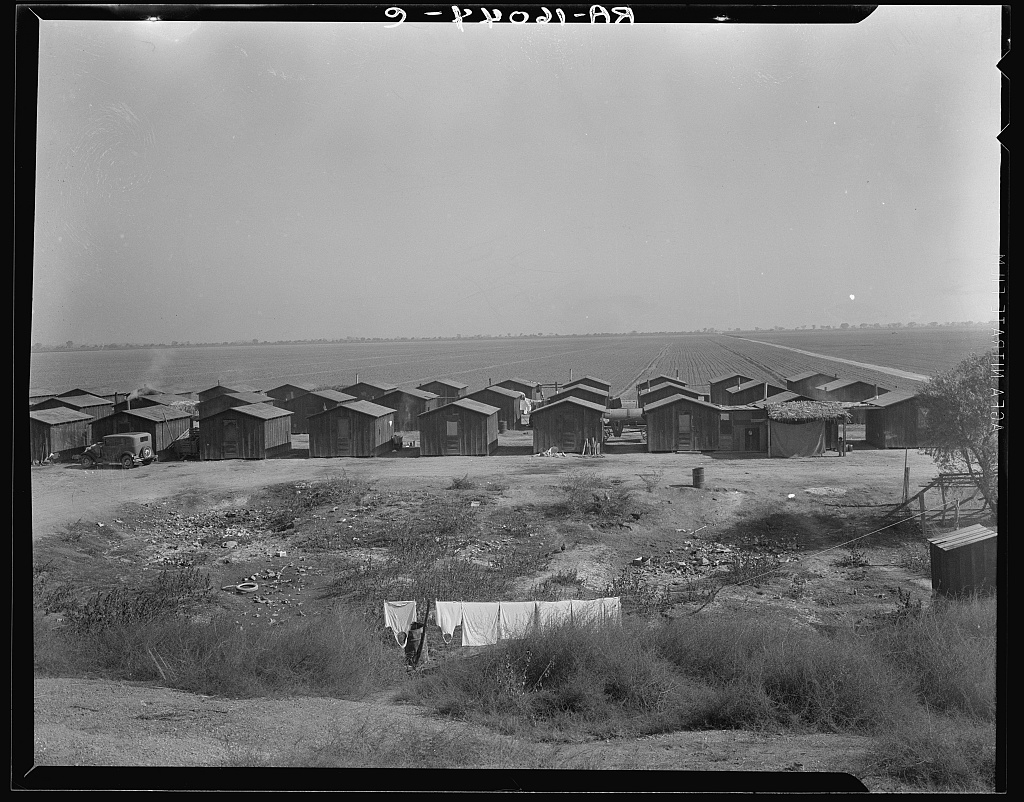 Rows of wooden company housing for cotton pickers south of Corcoran, California, with the open San Joaquin Valley in the background, 1936.
